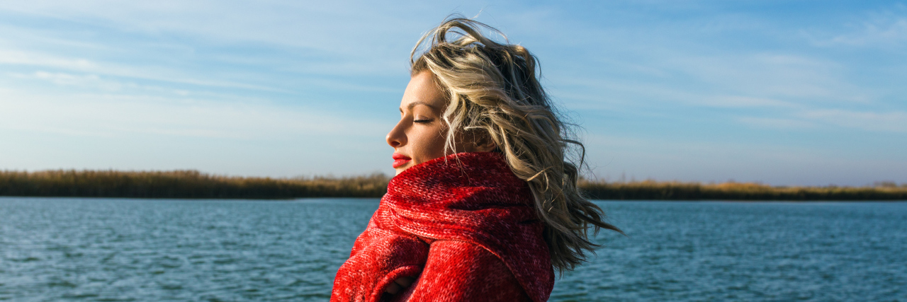 woman with blonde hair wrapped in a red blanket and standing in front of a lake