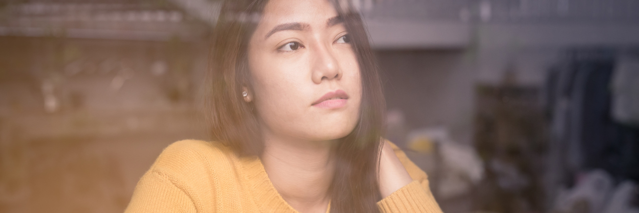 Lessons I Learned in the Psych Ward for Bipolar Disorder asian woman sitting alone at window contemplative