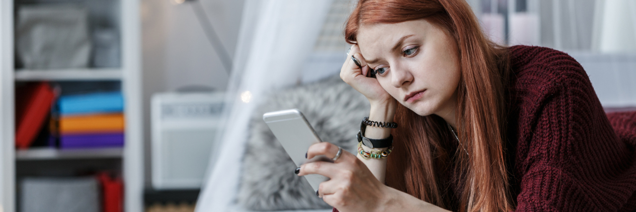 young woman lying on bed in room looking at phone