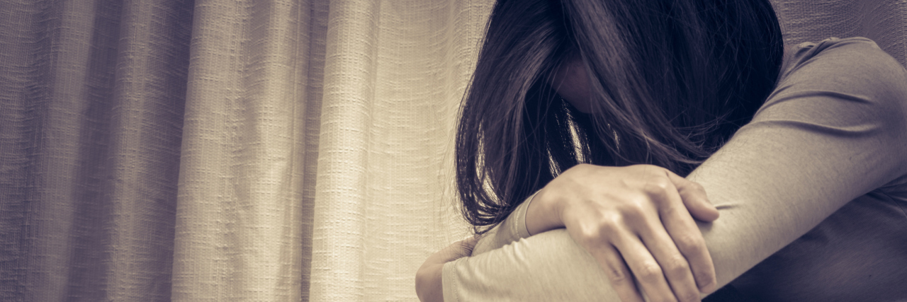 Why I Miss Being in a Psychiatric Ward asian woman alone in dark room with head buried in arms