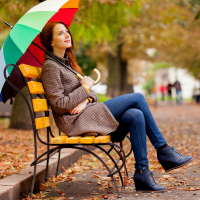 young woman sitting on park bench in fall with bright colored umbrella