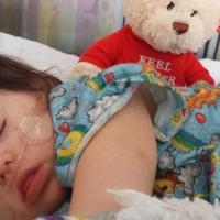 Little girl with Down syndrome sleeping at the hospital with teddy bear and oxygen