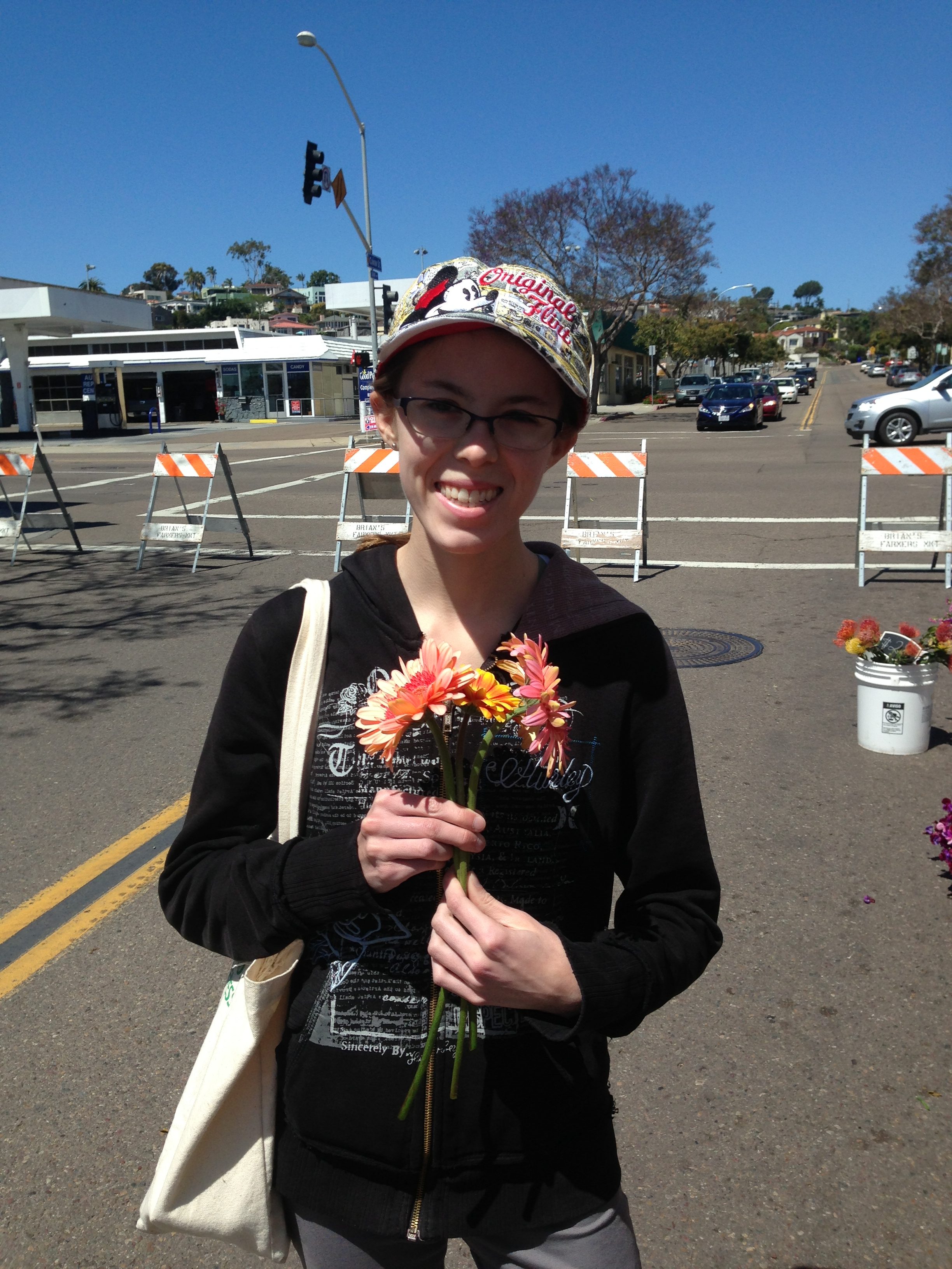 young woman wearing a hat and standing in a parking lot holding flowers