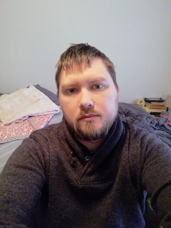 man wearing a brown sweatshirt and sitting on his bed