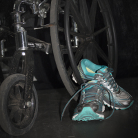 A pair of tennis shoes by a wheel of a wheelchair.