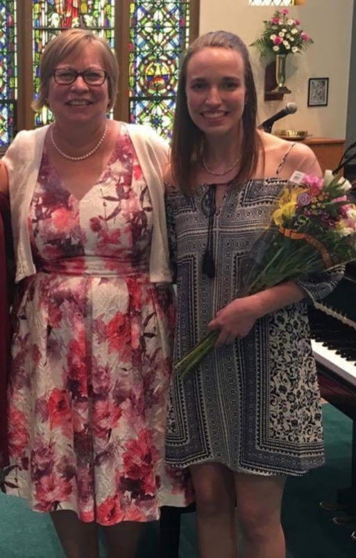 two women wearing dresses and stained in a church holding flowers