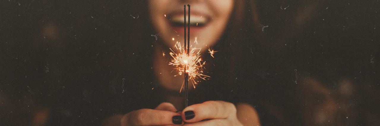 young woman laughing and holding sparkler with only sparkler in focus