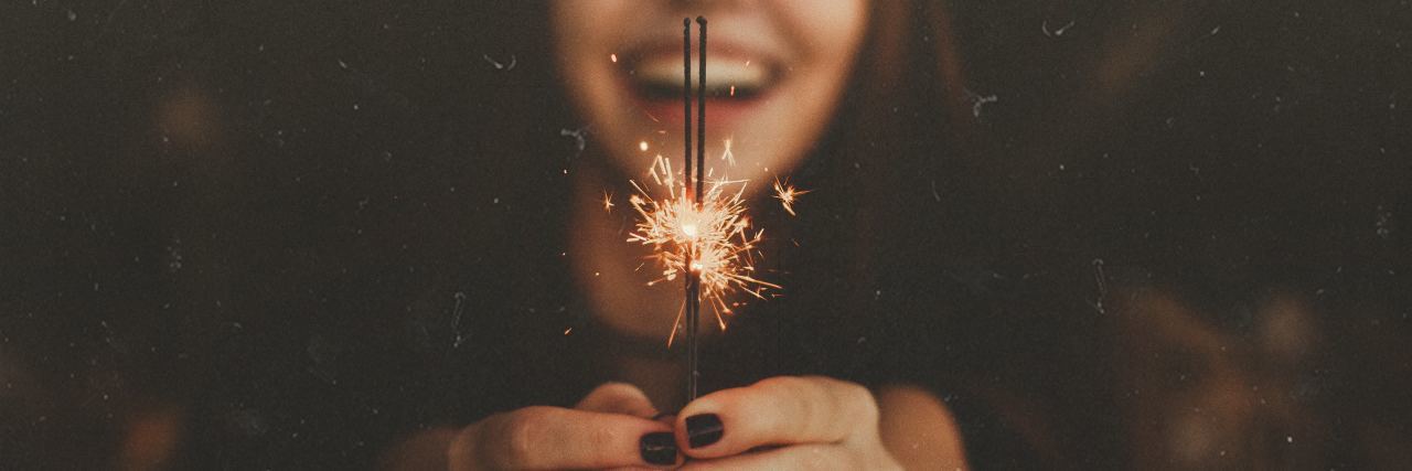 Alternatives to New Year’s Resolutions If You Live With Mental Illness young woman laughing and holding sparkler with only sparkler in focus