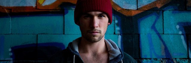 man wearing beanie standing in front of graffiti wall