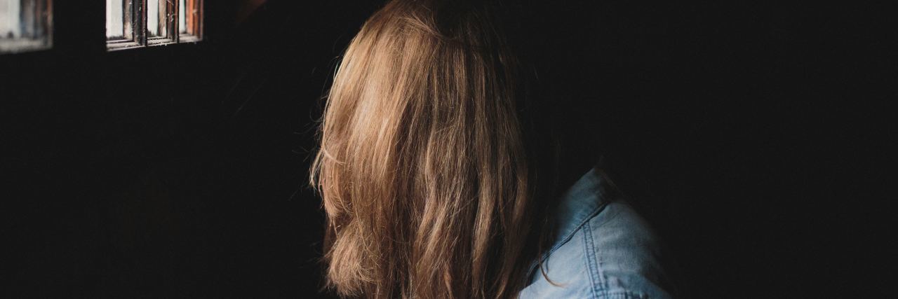 Tips for Accepting Help When You Live With Chronic Illness woman in a dark room with her hair covering her face