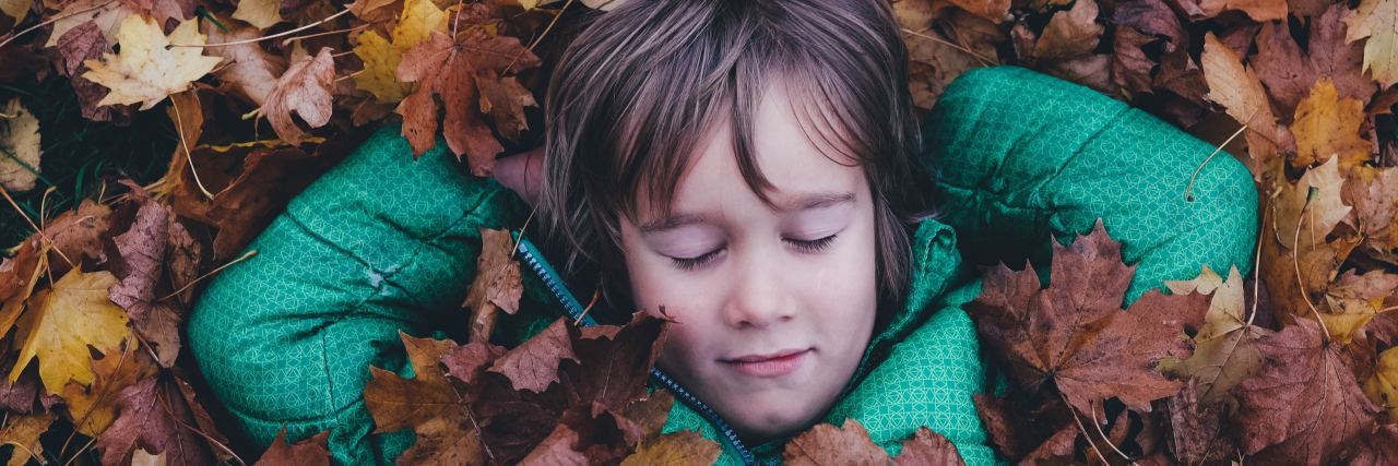 When Teachers Dismissed My Concerns About My Son's Development Boy with eyes closed laying in a pile of leaves
