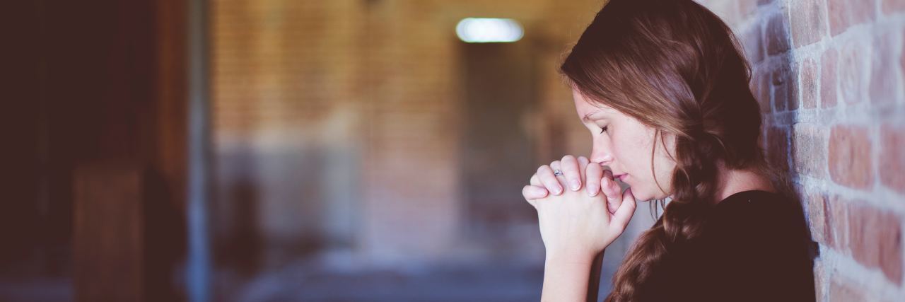 The Eating Disorder Thoughts That Still Haunt Me woman stands in hallway clasping her hands up to her mouth