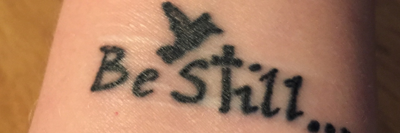 woman's tattoo that says "be still" with a cross and bird