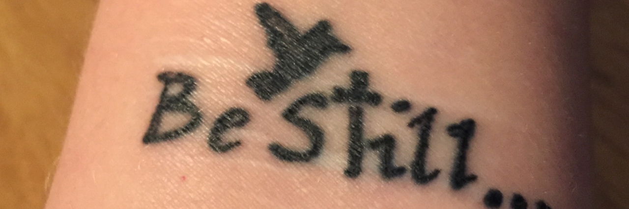 How My Tattoo Gives Me Hope as Someone Who Struggles With Self-Harm woman's tattoo that says "be still" with a cross and bird