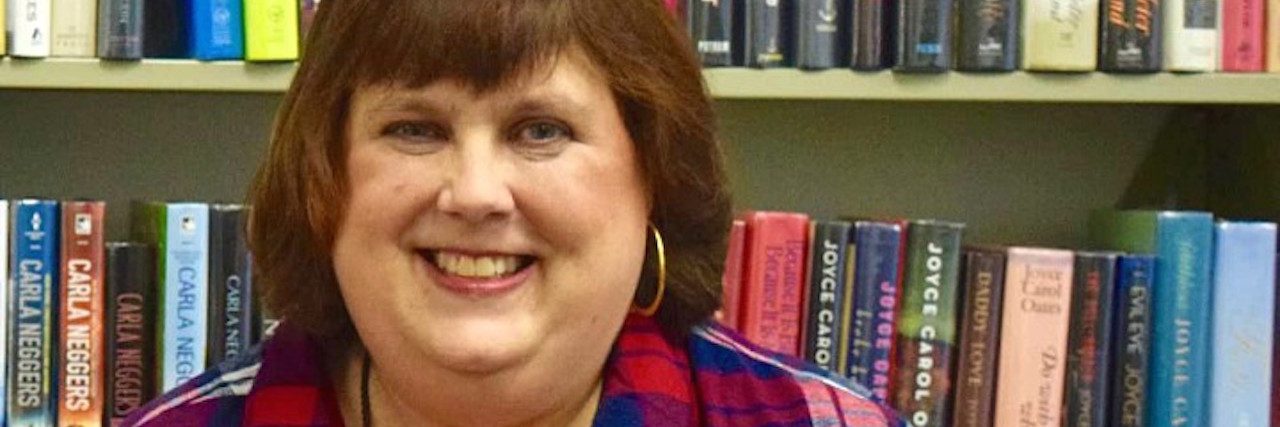 Myths About Ostomy Bags That Need Correcting A photo of the writer in a library, holding an illustration of a dog.