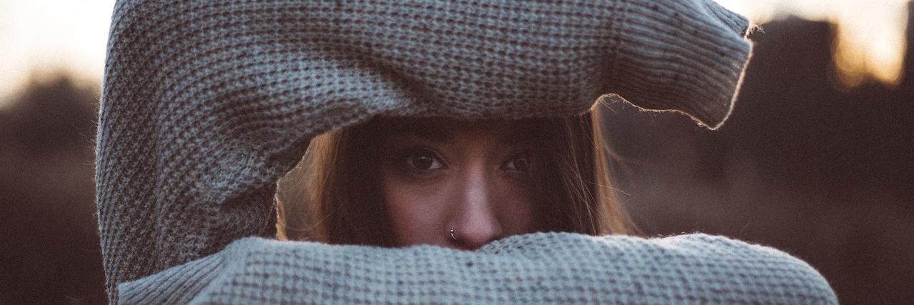 25 'Embarrassing' Symptoms of Borderline Personality Disorder Woman with arms covering top and bottom of her face, so only her eyes are visible, and she's looking directly at you.