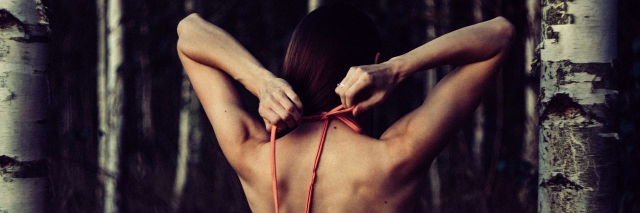 How the Debilitating Physical Side of Depression Affects Me woman with back to camera in forest tying dress with tension behind neck