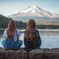 friends sitting in front of lake with mountain in distance