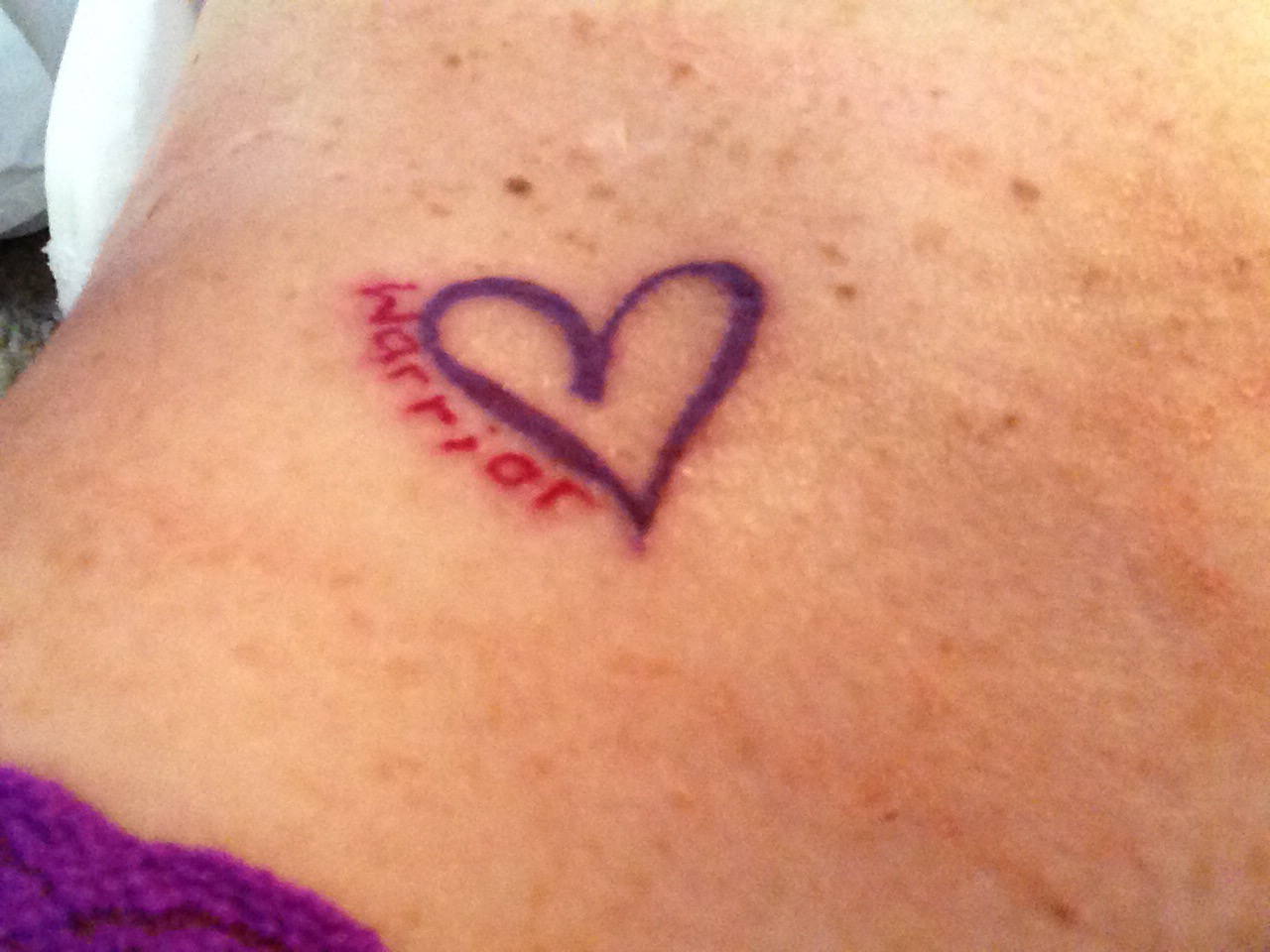woman's stomach with purple heart tattoo that says warrior