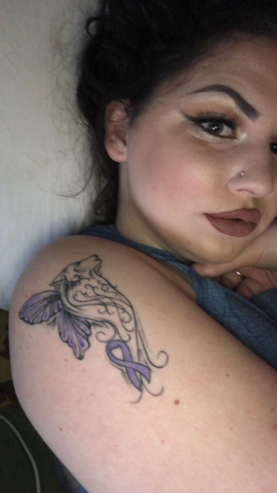 woman lying in bed with a purple awareness ribbon tattoo on her arm