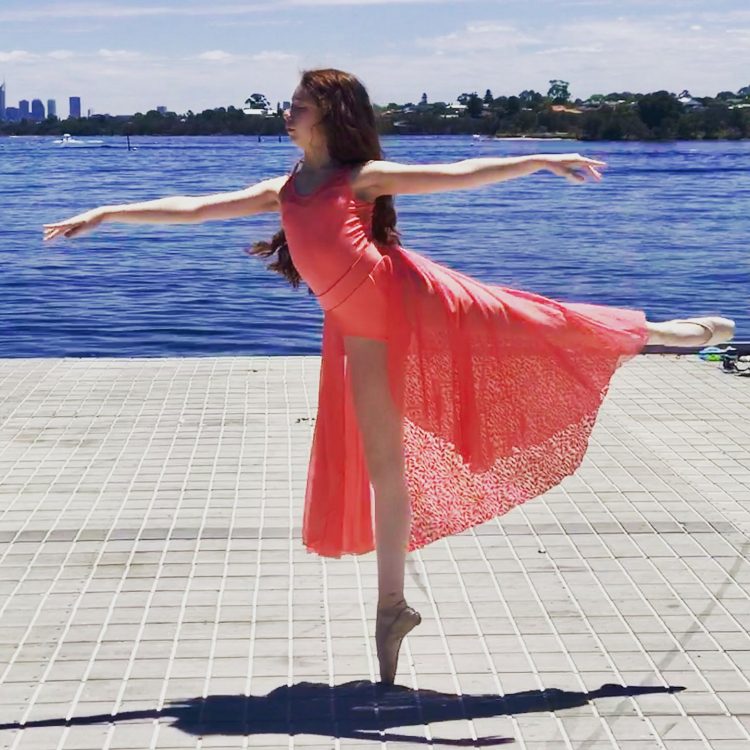 girl wearing pink dress and ballet shoes standing on one foot in ballet pose