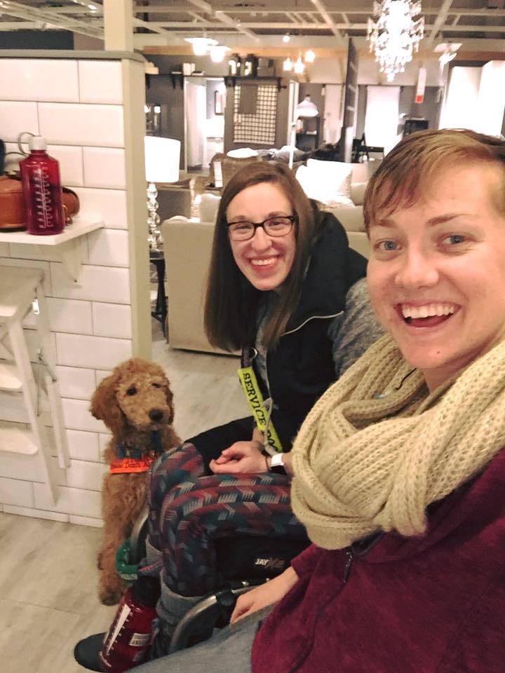 two women sitting in wheelchairs at ikea with one of the women's service dog in the background