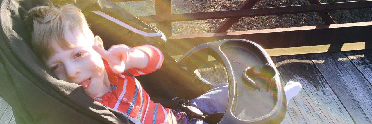 The Hallelujah Moments I Experience as I Parent My Child With CP Little boy sitting on a stroller and pointing at camera, sun rays seem to catch on him