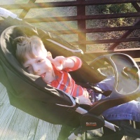 Little boy sitting on a stroller and pointing at camera, sun rays seem to catch on him