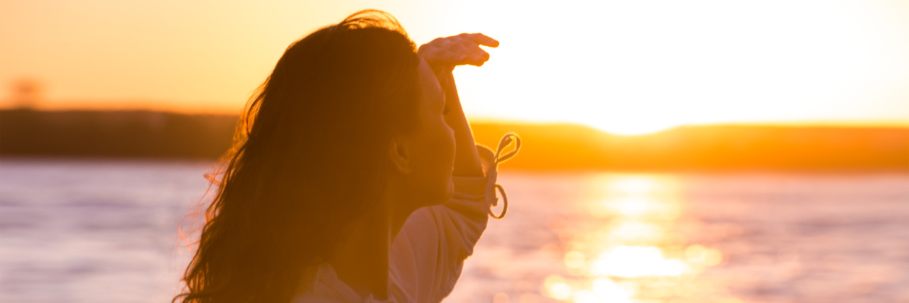 Coping With Chronic Illness Through Hope and Optimism woman looking at the sunset over a lake