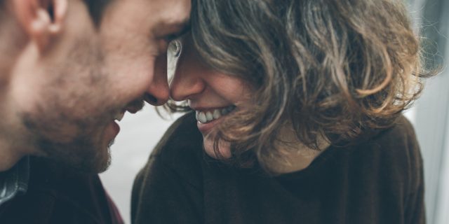 A woman and man looking at each other, foreheads touching, with a smile.