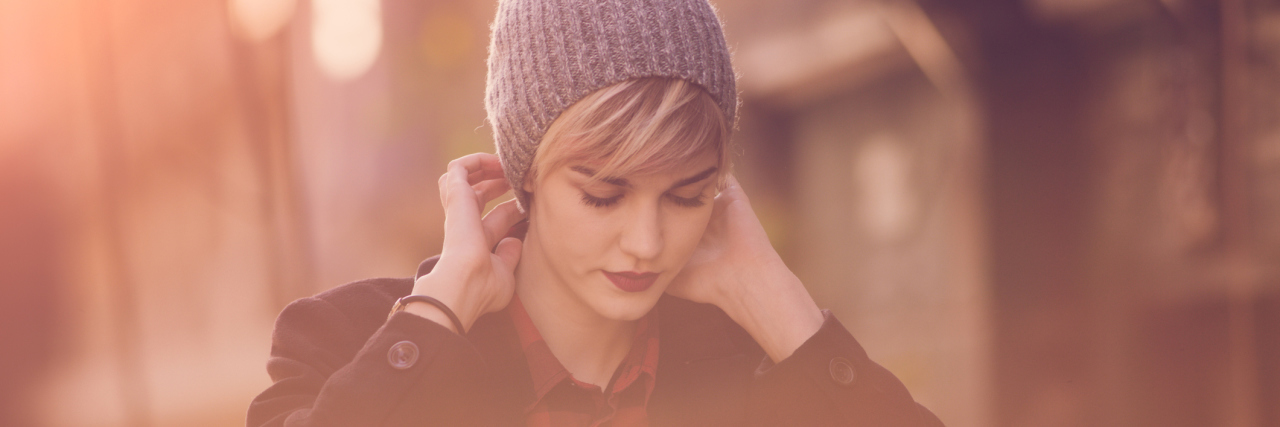 When Your Illness Makes You Break Society's Expectations A woman with short hair, wearing a hat, while walking down the street.