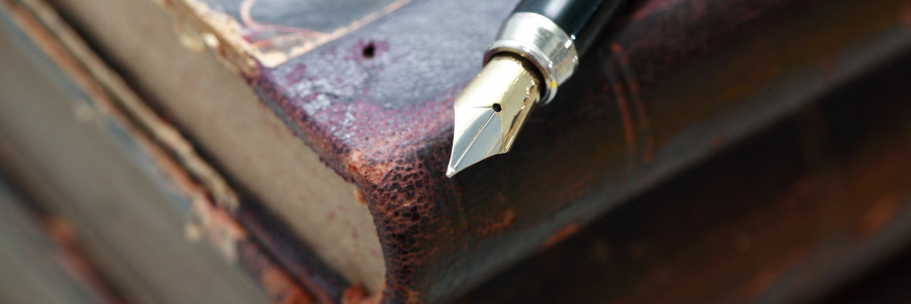 How to Write About a Character With Chronic Illness A pile of old books with a fountain pen on top.