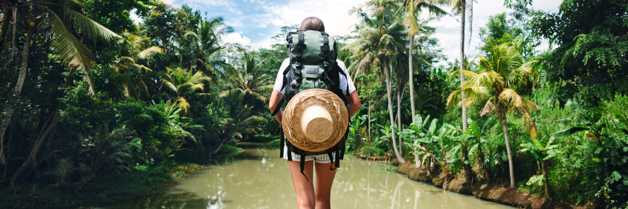 young woman traveling with backpack standing at edge of tropical river