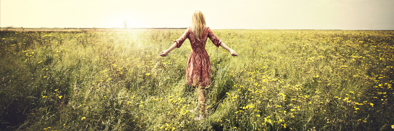 19 Lessons My Invisible Illnesses Have Taught Me A woman walking in a field, facing a way from the camera.