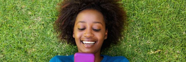 A woman laying on the grass, looking at her phone.