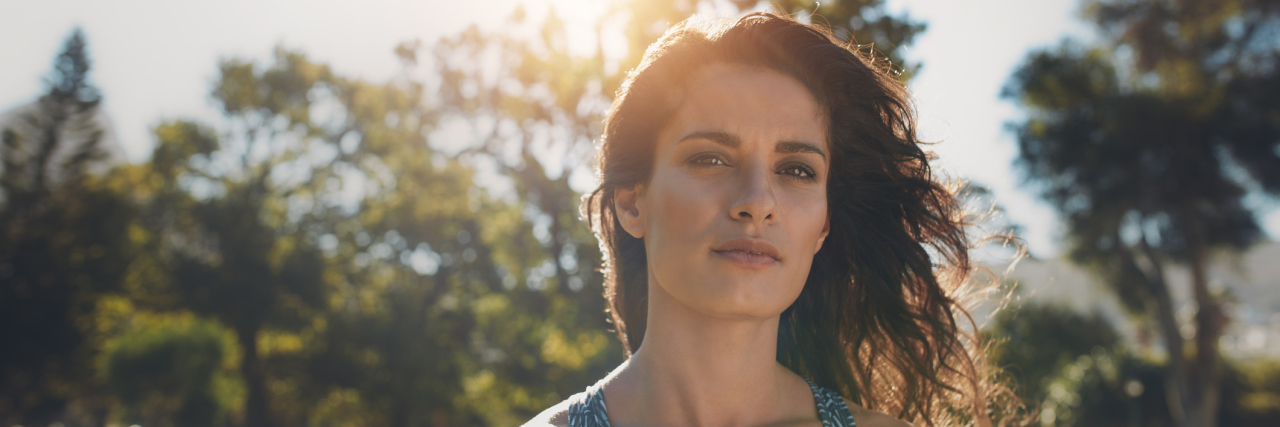 18 Lessons I've Learned After Living With Chronic Illness for 18 Years A woman outside in a park with a serious expression.