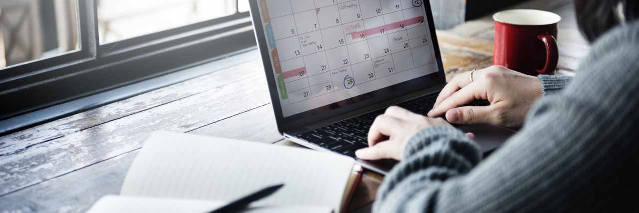 Tricks for Dealing With Brain Fog woman sitting at a cafe typing on a calendar on her computer next to an open journal
