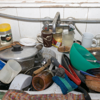 Pile of dirty utensils in a kitchen washbasin
