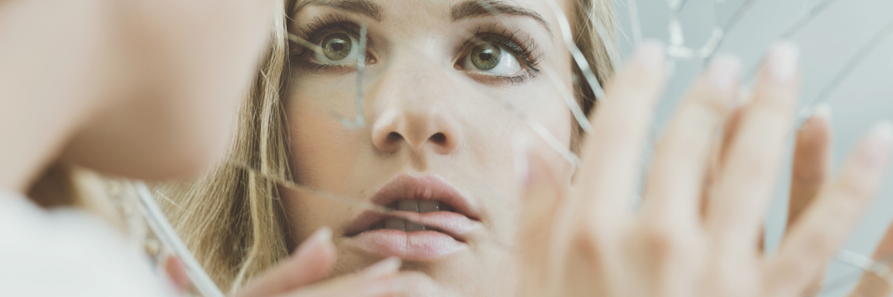 What the Journey Through Panic Disorder Feels Like young woman looking at her reflection in broken mirror