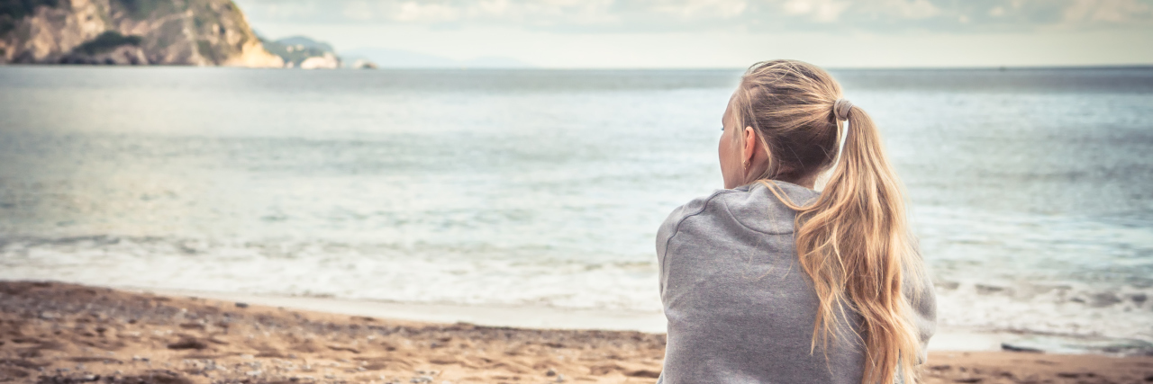 How I Found a New Purpose After My Diagnosis A woman sitting on the sand, looking out at a body of water.