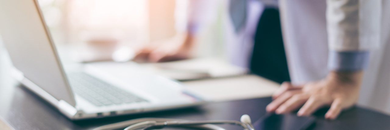 When Doctors Dismiss Pain Because You Look 'Normal' doctor standing over his desk with a computer and stethoscope on the table