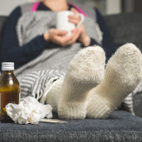 A woman with her feet propped up with tissues and medicine surrounding her.