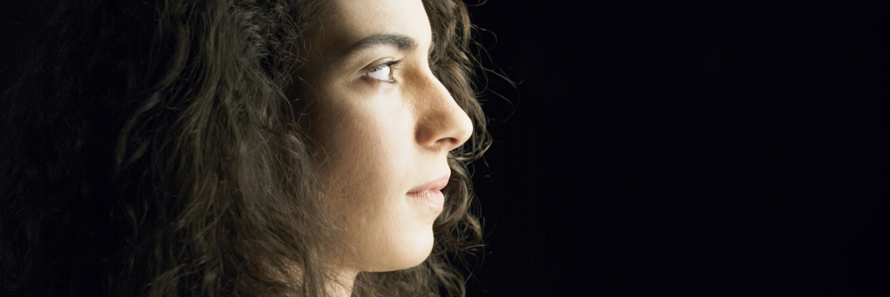 The Problem With Thinking Negativity Causes Chronic Illness profile of a woman with dark curly hair looking to the right