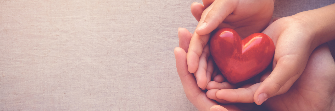 Adult and child hands holding red heart.