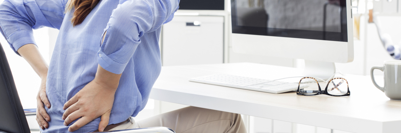 When Multiple Doctors Can't Diagnose Your Chronic Back Pain A woman with back pain sitting at her computer