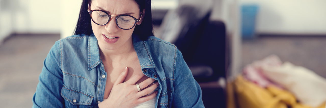 How Anxiety Led to My Dysautonomia Diagnosis woman sitting at a desk and clutching her chest in pain