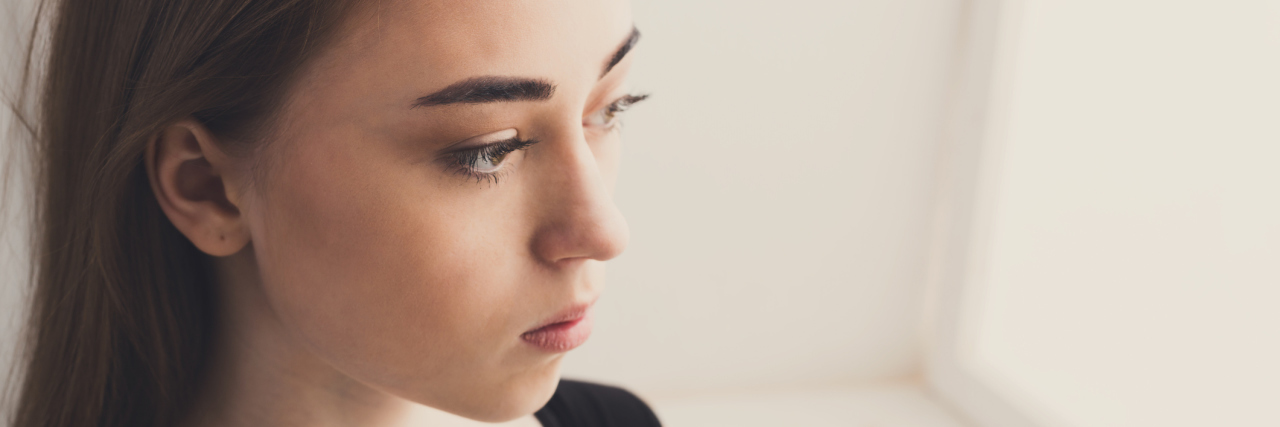 When Remission Feels Like a Waiting Game A woman with a serious expression looking out a window.