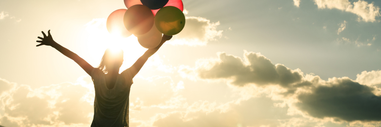 How I’m Pushing My Anxiety’s Boundaries This Year woman in grassland with colourful balloons against sun