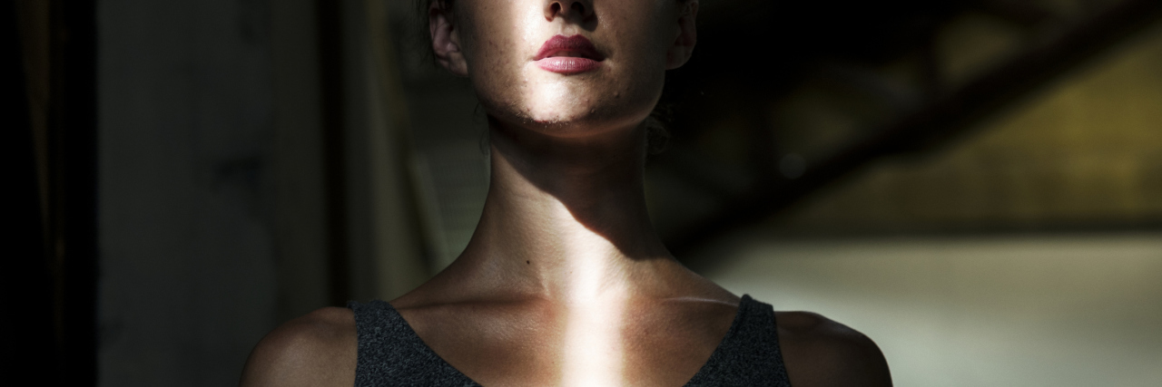 The Fine Line Between Health Advocacy and Illness Shaming A woman in the dark, with a line of light shining on her.