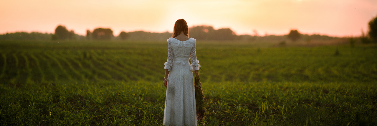 The Stained Dress -- a Work of Fiction Young woman in long white lace dress on cornfield at sunset. Back view.